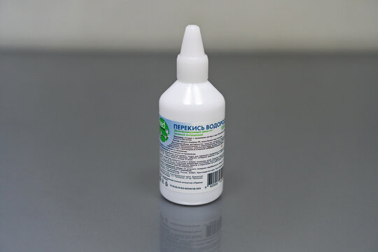  White bottle of 3% Hydrogen Peroxide solution on table on gray blurred background. White bottle of hydrogen peroxide on gray table background. Products for antiseptic. 