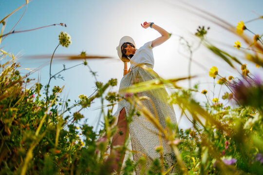 Summer mood. a young and cheerful girl posing against a background of blue sky and flowers. girl dancing among flowers.