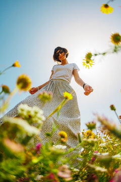 Summer mood. a young and cheerful girl posing against a background of blue sky and flowers. A beautiful girl dances among flowers. Happy girl among blooming flowers, outdoors.