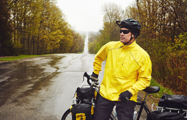 Naklejka premium Travel, man and break with touring bicycle in nature for exploring, bikepacking and winter adventure. Cyclist, mature person and relax with bike on wet road for sightseeing, cycling rest and freedom
