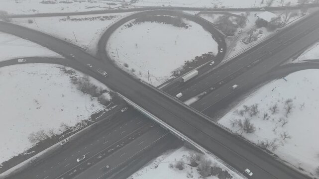 4K 60fps aerial static top view of a highway cloverleaf interchange in winter fog, cinematic grainy atmosphere.