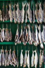Close Up View of Traditional Salted Dried Fish Hanging on Green Wooden Racks at a Local Street Market