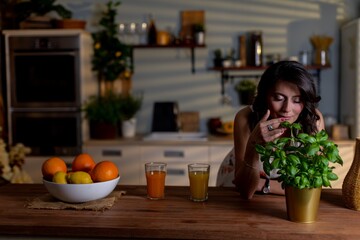 Relaxed woman with herb in kitchen, Serene woman rests in modern kitchen holding fresh basil, Calm female figure lounges at counter with steaming mug and potted plant