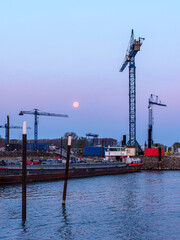 Obraz premium Cranes and full moon over industrial harbor at dusk