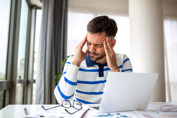 Fototapeta premium Stressed Man Holding Temples with Both Hands Suffering from Severe Migraine and Headache While Working at Laptop. Concept of Chronic Pain, High Pressure, Professional Burnout and Mental Health.
