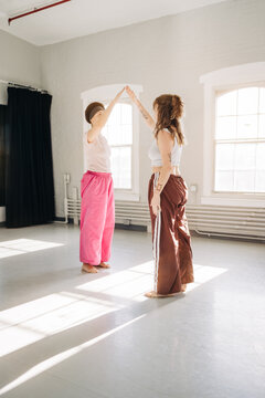 Two dancers high-five in sunlight during studio practice