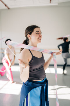 Smiling dancer twirls pastel ribbon in sunny studio practice