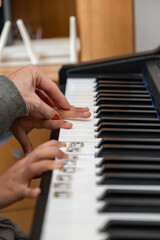 Fototapeta premium Adult hand with red nail polish guiding child's hand on piano keys, teaching music during an educational lesson