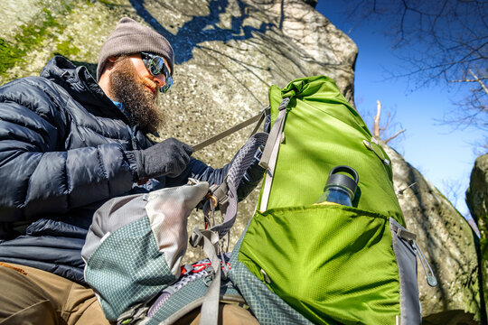 Bearded hiker adjusting green backpack during mountain trekking break