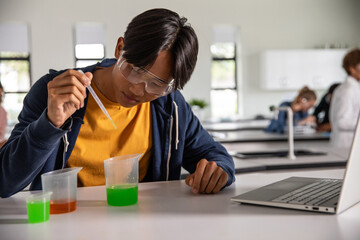 Diverse classmates conducting science experiment using plastic dropper and beakers at lab bench