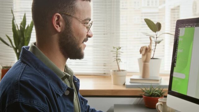 Medium close-up of hands and face of cheerful polyethnic young male UX developer drawing mobile application wireframes using graphic tablet, glove and stylus, viewing on large monitor