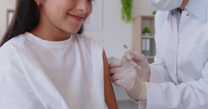 Masked clinician gives a vaccine injection into a young childs arm at a pediatric clinic visit, using sterile gloves and syringe. Doctor pediatrician vaccinating patient for immunity. Vaccination.
