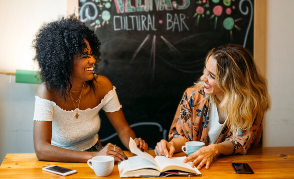 Diverse women friends laughing reading a book in cafe