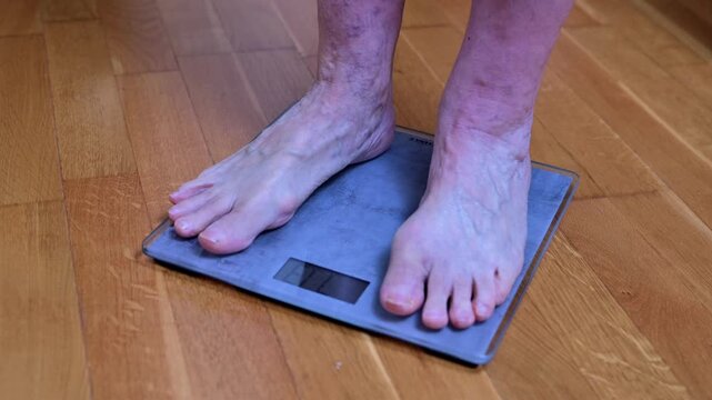 Person Stands On Blue Digital Weight Scale On Wooden Floor In Home Setting