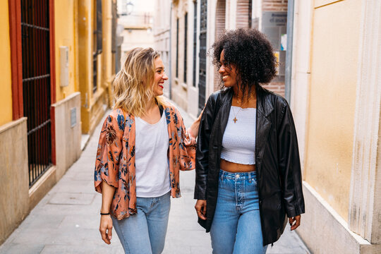 Diverse young women friends walking laughing in urban alley
