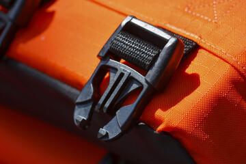 Secure black plastic buckle and clasp on an orange strap. close up detail of outdoor safety equipment with strong fastener, symbol of preparedness for adventure