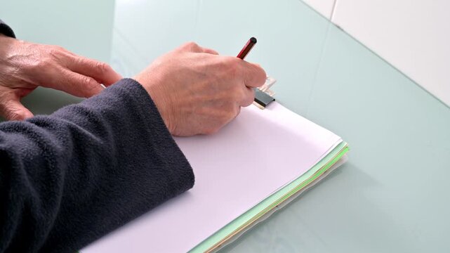Close-Up Of Hand Writing On Blank Paper With Clipboard At Desk For Study Or Work