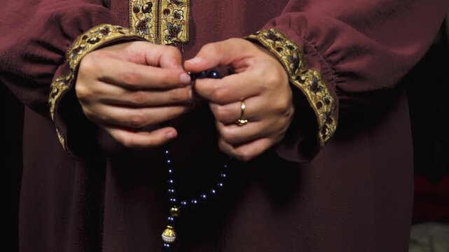 Muslim woman's hand holding blue prayer beads or tasbih and counting them with her finger. Islamic concept for dhikr or zikr recitation