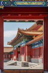 Fototapeta premium The Forbidden City,Traditional Chinese palace architecture viewed through a red wooden doorway with ornate roof details and vibrant colors.