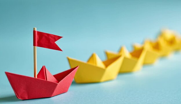 Red origami paper boat with small red triangular flag on wooden toothpick leading a row of yellow origami paper boats, all arranged in diagonal line on light turquoise blue surface