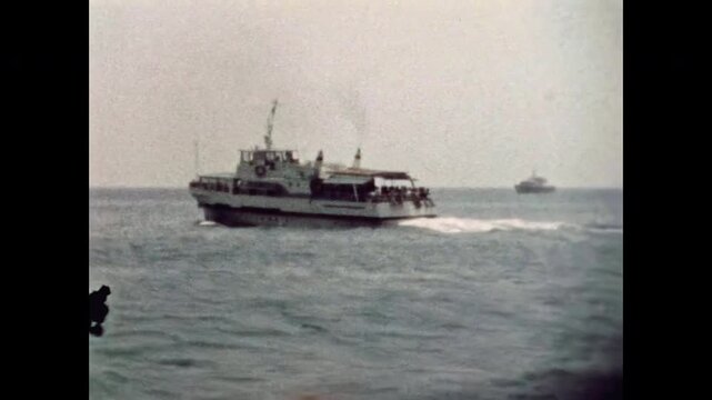 Wide view of a passenger steamship sailing away into deep blue sea on sunny day. Vessel departing from coastline. Maritime travel in summer journey. Old film. Archival retro 1970s. Vintage archive