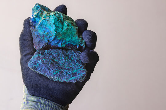 Hand with safety glove holding malachite and chrysocolla ore against tan background. Source of Copper (Cu) metal. Mine, mining. Copy space