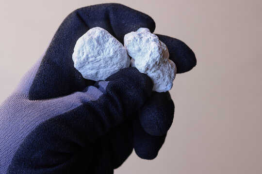 Hand with safety glove holding Magnesite ore against tan background. Source of magnesium oxide (magnesia) for refractory bricks and magnesium metal. Mine, mining