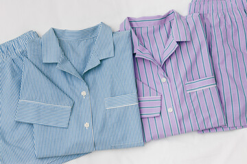 Violet blue Pajamas folded on white bedclothes background. Top view stylish man and woman sleepwear with natural fabric texture. Cozy striped pyjamas for sleeping, concept of rest, healthy sleep.