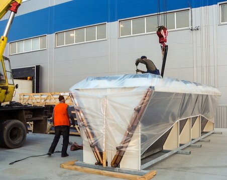 Workers prepare a large industrial chiller for transport outside of a manufacturing facility.