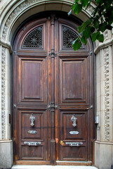 Ornate wooden double doors with arched windows. Close-up of elegant double wooden doors with decorative iron lattice windows and arched glass panels, set in a stone facade.