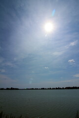 薄雲から輝く太陽と池の風景
