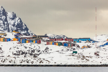 Wide coastal panorama of Sisimiut with colorful Inuit houses, snow covered terrain and steep arctic mountains rising above the calm fjord, Greenland © vadim.nefedov