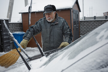 Man clears snow from car windshield in winter at home in the early morning hours