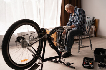 Obraz premium Senior elderly man repairing examined and maintained his damaged bicycle at home.