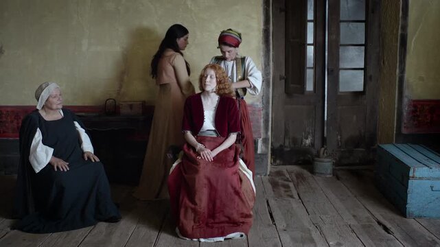 Actors engage in a historical role play while wearing costumes from a different era. The setting includes a simple room and wooden flooring, creating an authentic atmosphere for their performance.