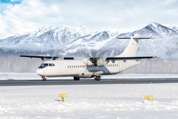 White passenger turboprop airplane on the runway at a winter airport on the background of high snow capped mountains