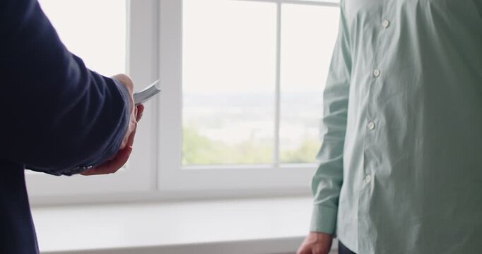 Bribe money cash exchange symbolizes corruption. A discreet payoff between men by a window, as a cash bundle moves hand to hand, implying kickback, extortion. Clear concept illicit cash bribe.