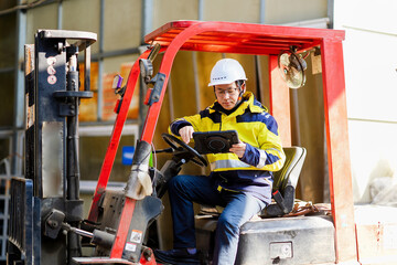 Worker operating a tablet while driving a red forklift in a warehouse © zhu difeng