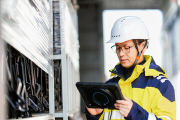 Worker wearing safety helmet holding tablet while inspecting equipment cabinet on site © zhu difeng