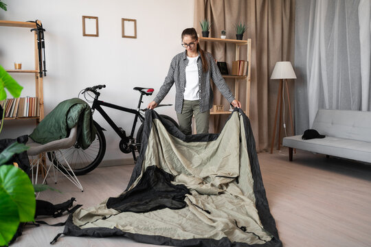 Young woman traveler packing camping tent while preparing for hiking trip at home
