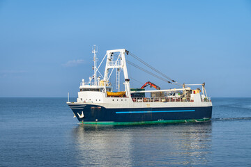 Obraz premium Working trawler underway on open sea near Inis Mor Island, Galway in Ireland. Deck cranes and winches poised for net deployment. Calm water with gentle ripples, distant coastline on horizon