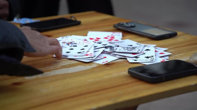 Scattered playing cards and smartphones on a wooden table surface