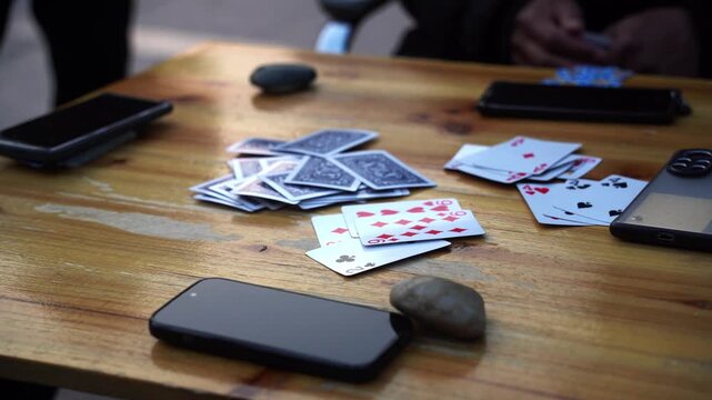 Scattered playing cards, smartphones, and a stone on a wooden table surface