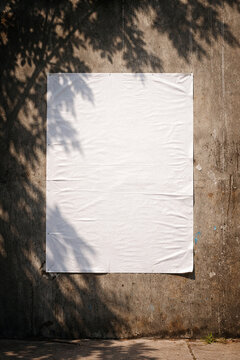 Blank white poster paper glued on a weathered grey concrete wall mockup with urban street shadows.