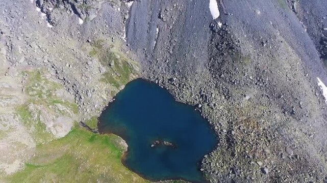 Aerial view of alpine lake surrounded by tundra meadows in the Rocky Mountains at high altitude. Clear summer light reveals rugged peaks and pristine wilderness across remote American ranges.