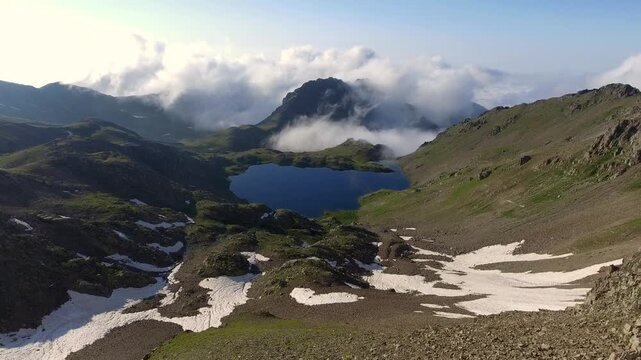 Aerial view of alpine lake surrounded by tundra meadows in the Rocky Mountains at high altitude. Clear summer light reveals rugged peaks and pristine wilderness across remote American ranges.
