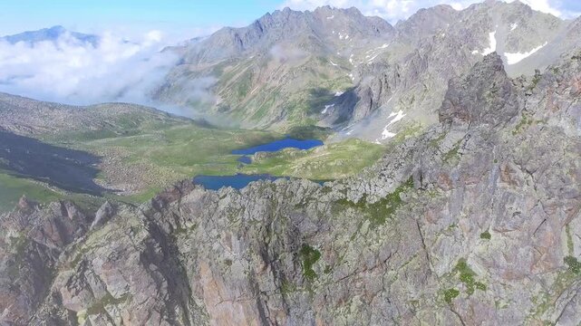 Aerial view of alpine lake surrounded by tundra meadows in the Rocky Mountains at high altitude. Clear summer light reveals rugged peaks and pristine wilderness across remote American ranges.