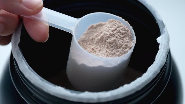 A woman scooping chocolate whey protein powder from a container. Close up.