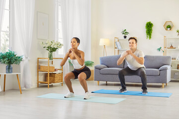 Fototapeta premium Couple family workout at home together. They practice exercise with squats and light cardio on mats, training legs, staying healthy and boosting fitness. Shared goals nurture a strong bond.