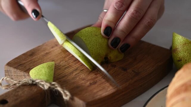 hand slicing pear into thin pieces on wooden cutting board. Close-up 